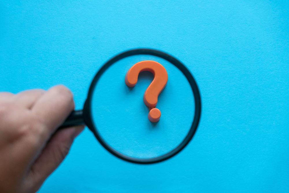 A hand holding a magnifying glass over a question mark